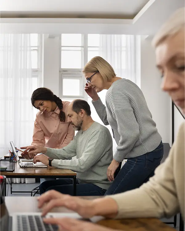 Uma foto de uma sala de aula moderna, com um instrutor orientando um grupo de alunos em computadores, transmitindo a ideia de aprendizado presencial e prática.